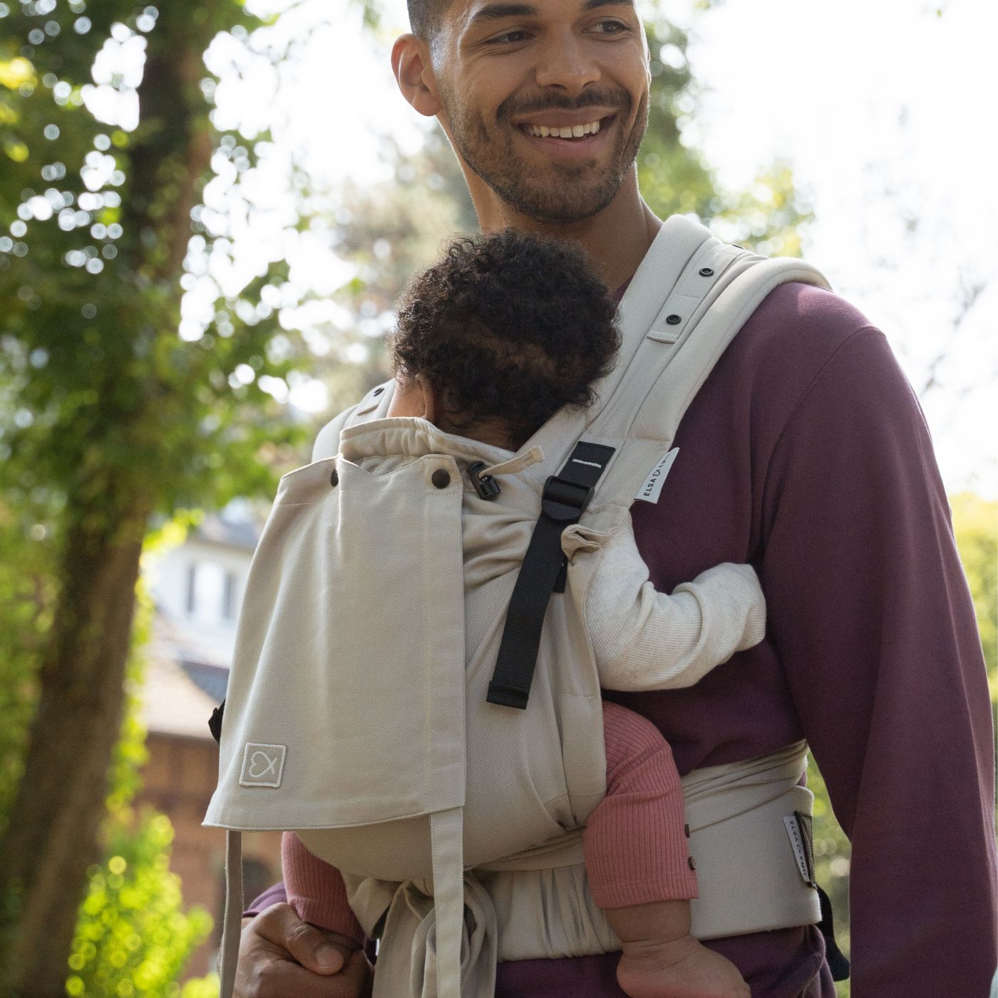 Vater trägt sein Baby mit der Halfbuckle in #farbe_kängurubeige