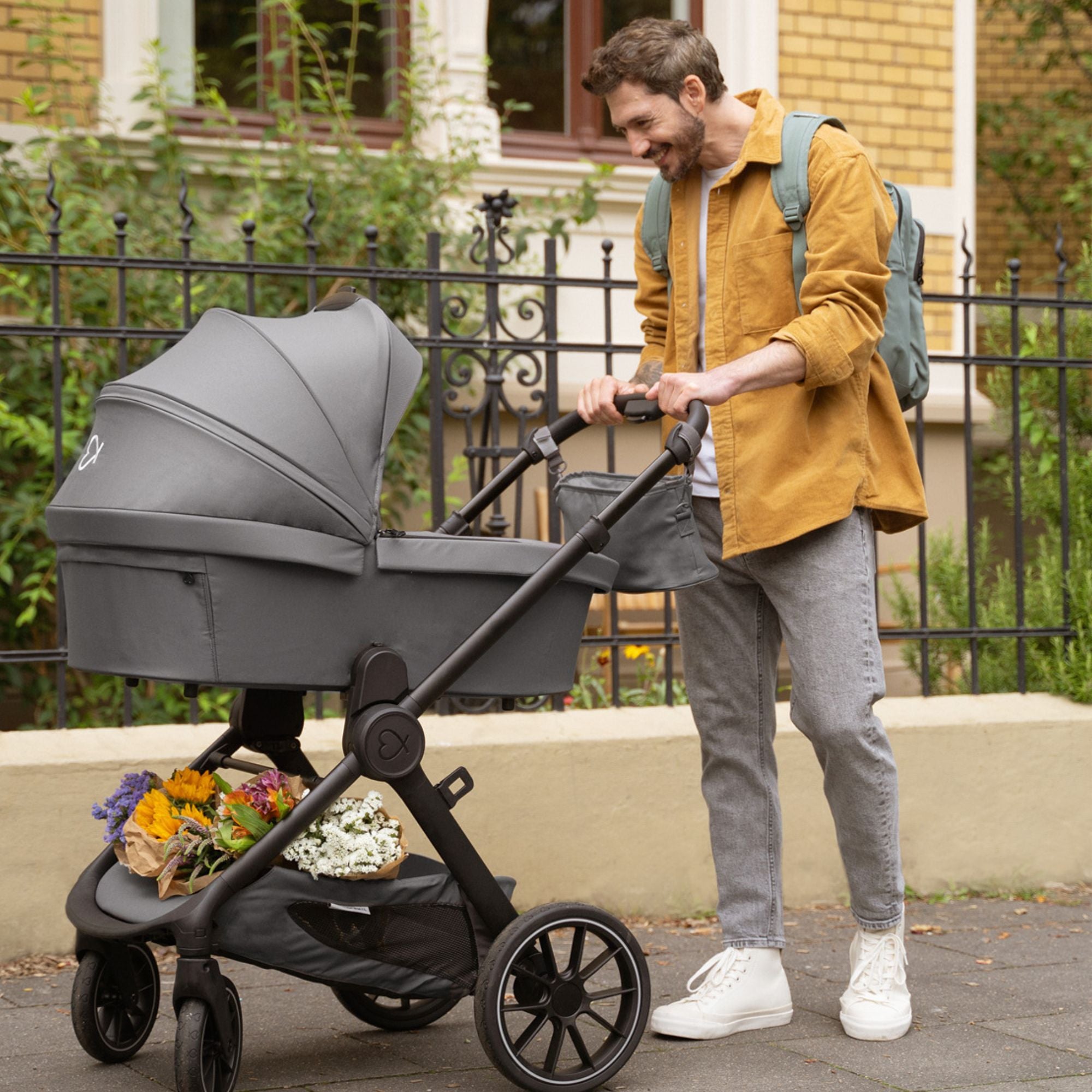 Vater mit Kinderwagen in #farbe_elefantengrau und Henkelrucksack in #farbe_krokodilgrün