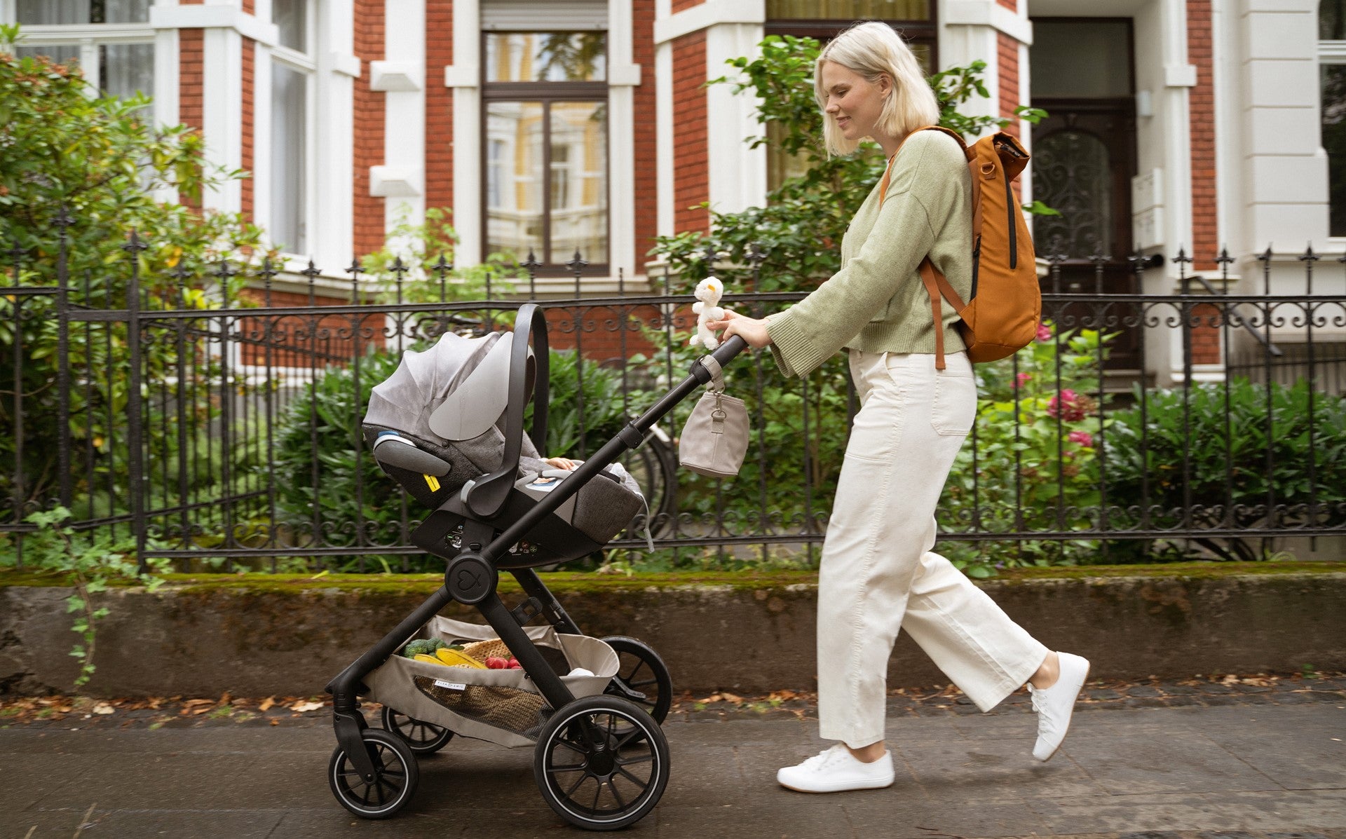 Mama spaziert mit einer Babyschale auf dem Kinderwagen