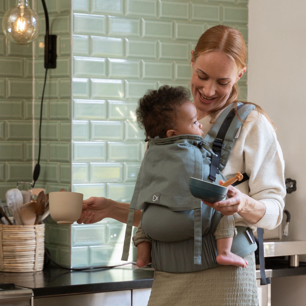 Mutter trägt ihr Baby mit der Fullbuckle in #farbe_krokodilgrün und hat dabei alle Hände frei