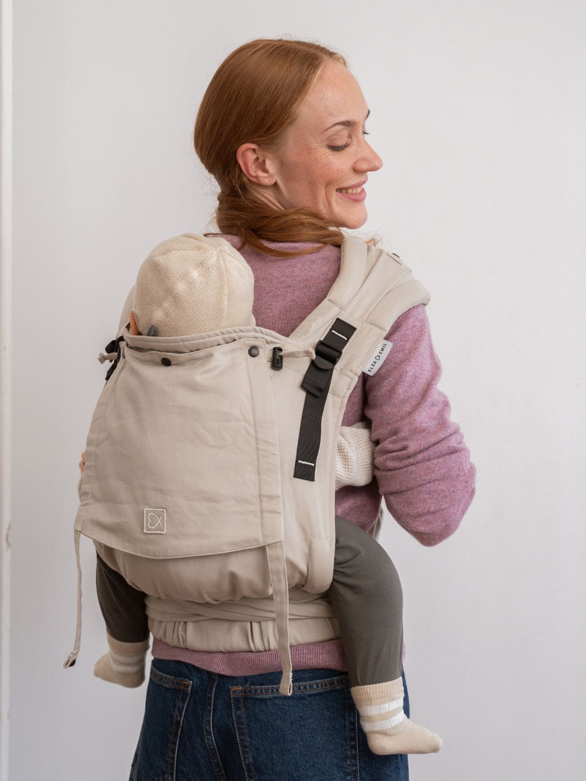 Mutter trägt das Baby mit der Halfbuckle in #farbe_kängurubeige auf dem Rücken